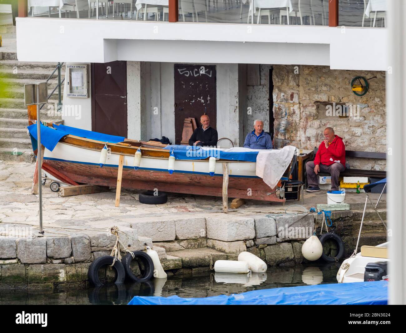 Mediterranean senior male people sitting seated chatting near wooden boat harbor port Lovran Croatia Europe Stock Photo