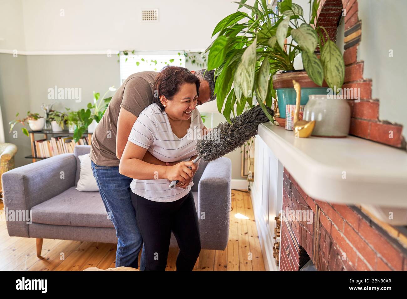 Affectionate playful mature couple with duster dusting living room Stock Photo