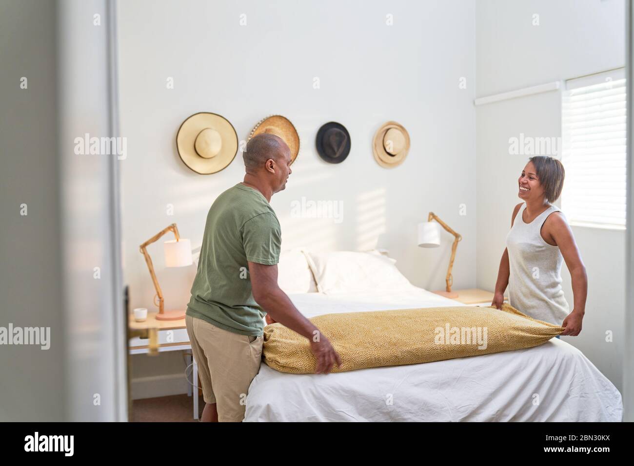 Couple making bed in bedroom Stock Photo