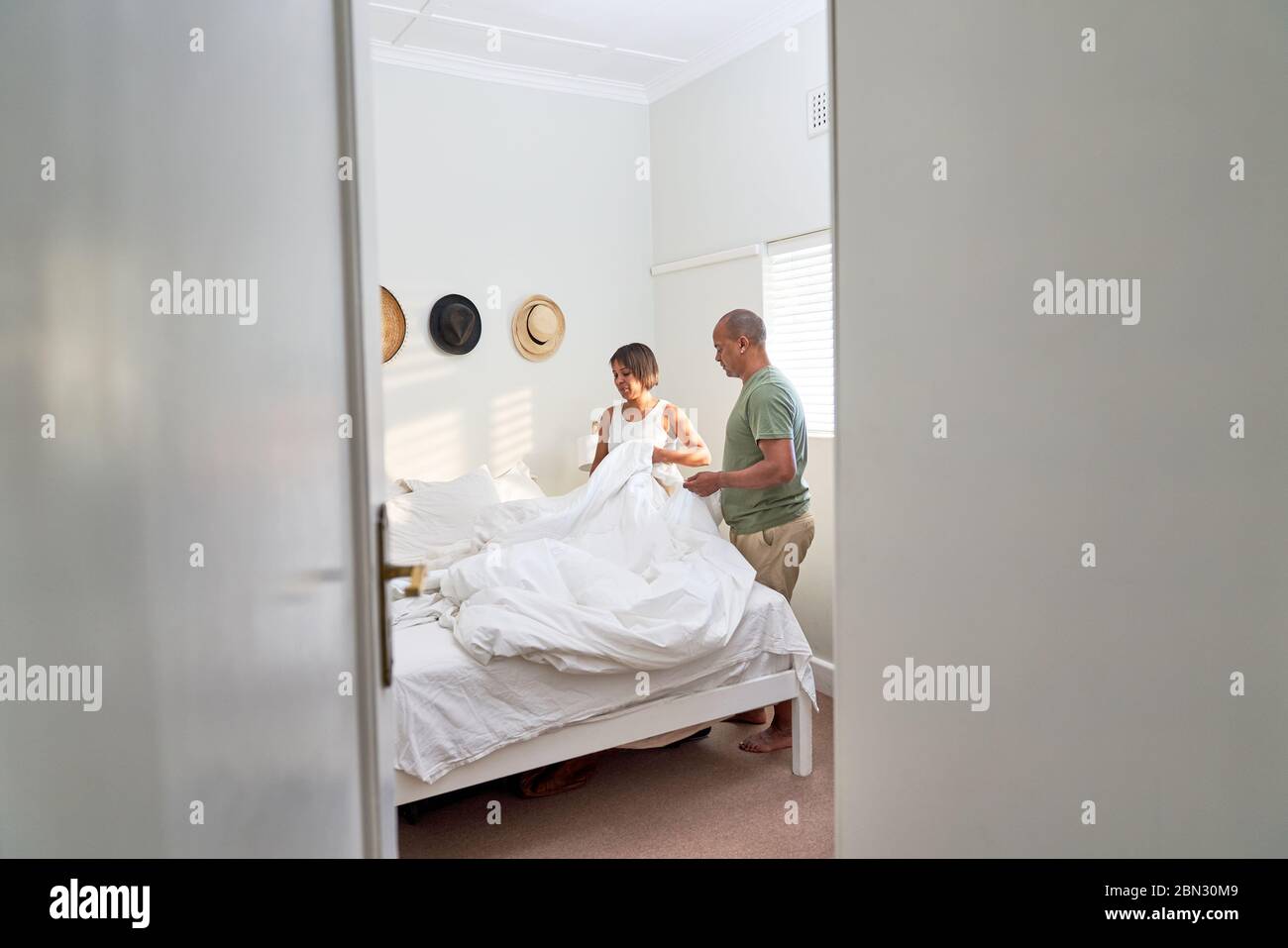 Couple making bed in bedroom Stock Photo