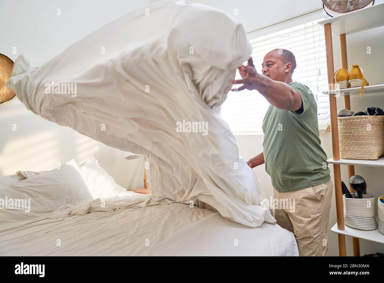 Man with duvet making bed in bedroom Stock Photo