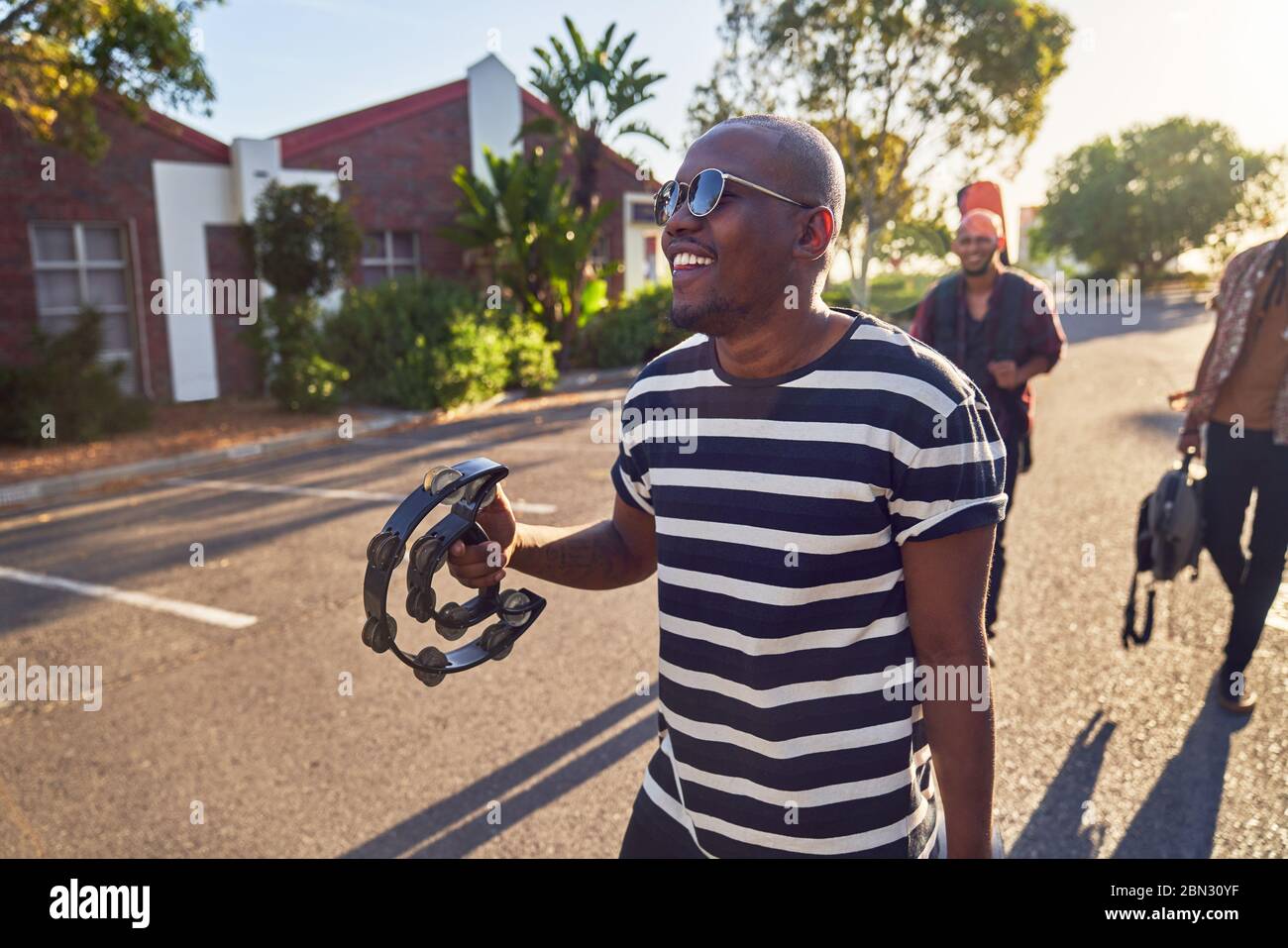 Happy young male musician with tambourine on sunny street Stock Photo