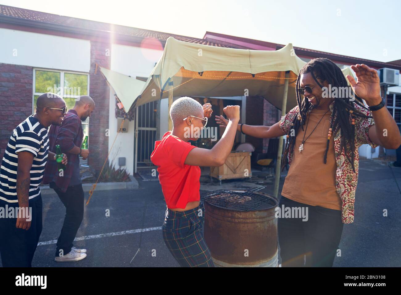 Carefree friends dancing and barbecuing in sunny parking lot Stock Photo