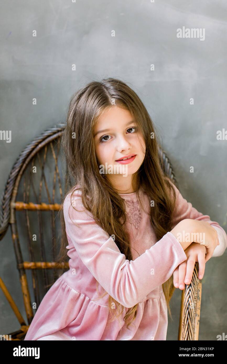 Pretty small girl in beautiful pink dress sits on the wooden chair and ...