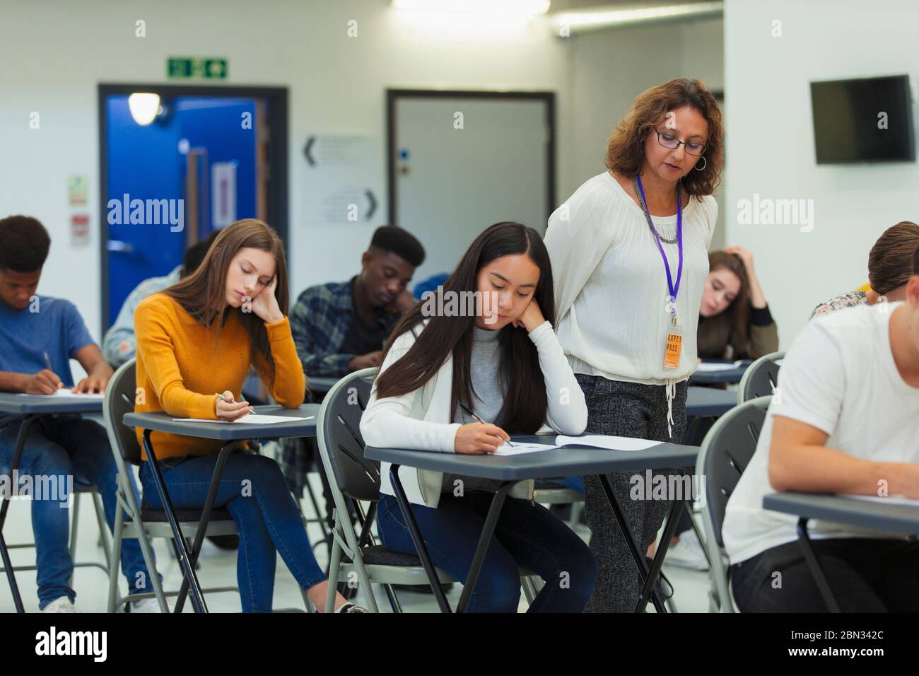 High school teacher supervising students taking exam at desks Stock Photo