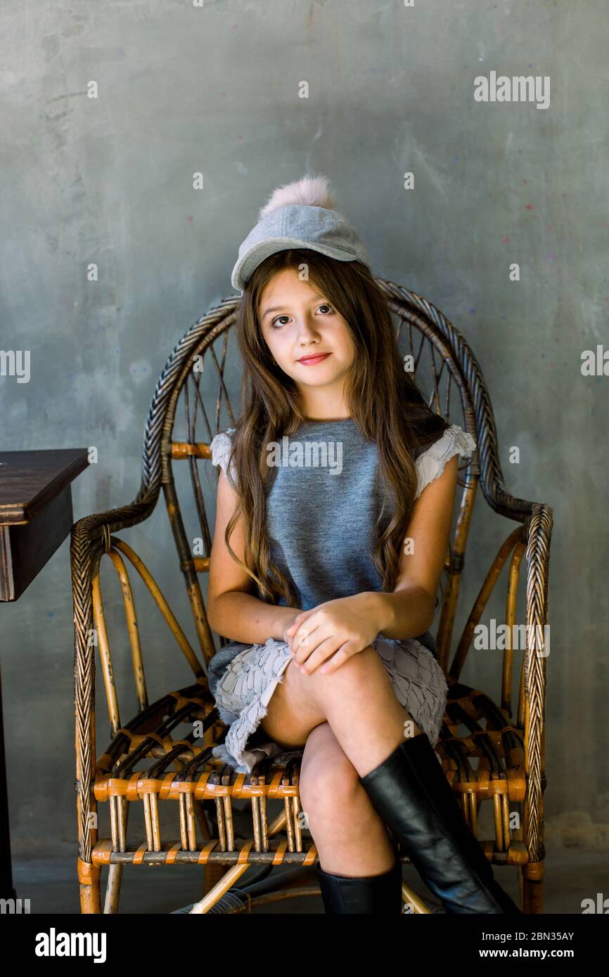 Shot of beautiful brunette Caucasian little girl wearing grey dress and with a hat looking at the camera with adorable smile sitting on a wooden Stock Photo Alamy