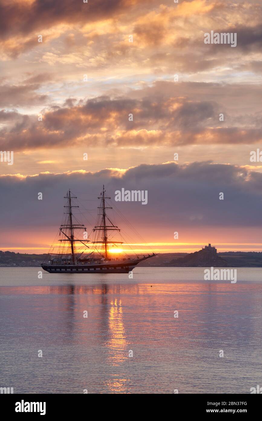 A tall ship anchored out in Mounts Bay at sunrise with St Michael's Mount in the distance Stock Photo