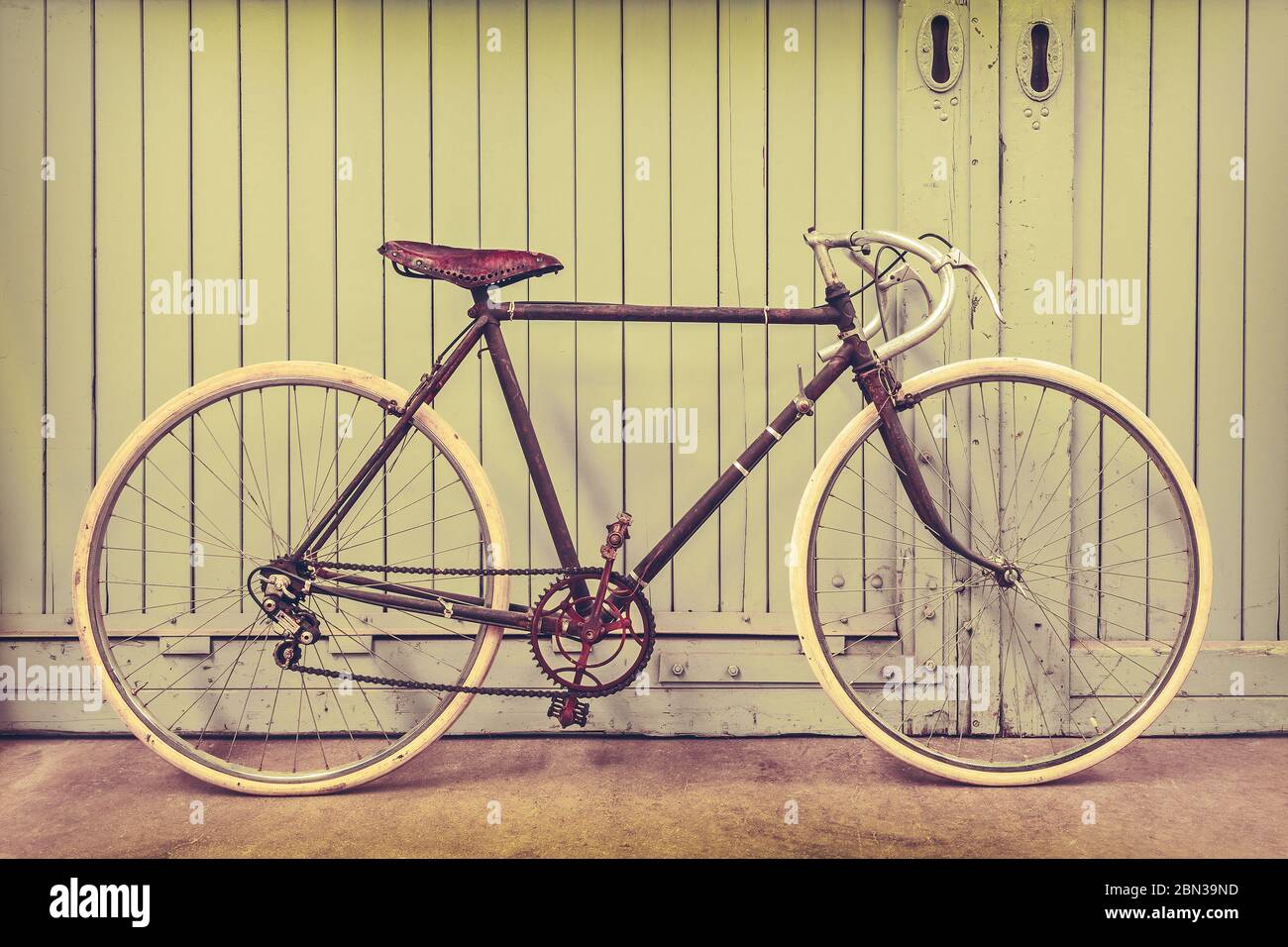 Retro styled image of a rusted racing bicycle parked in an old factory with wooden doors Stock Photo