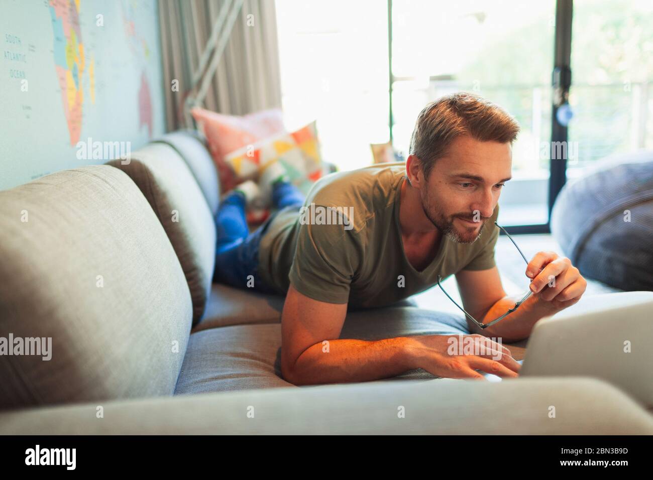 Man relaxing, laying on sofa using laptop Stock Photo