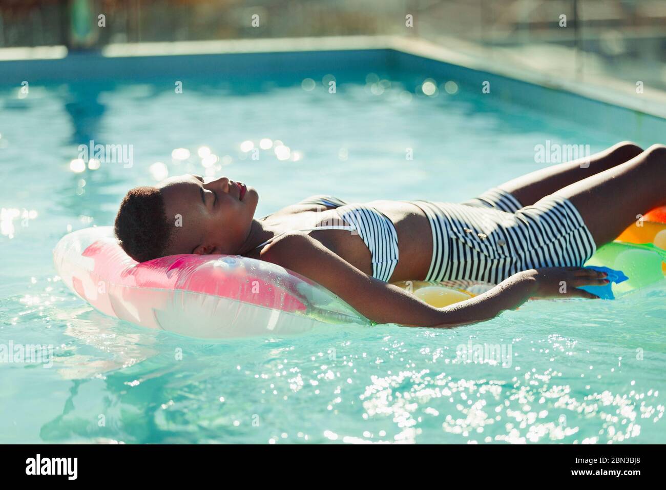 Serene young woman laying on inflatable raft in sunny swimming pool Stock Photo