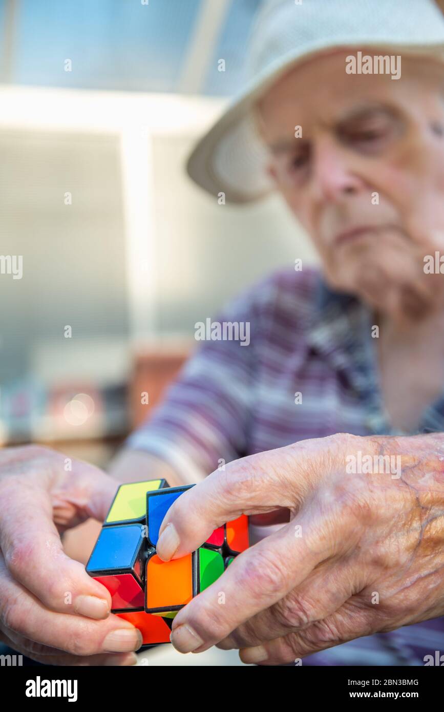 Elderly man uses a cube puzzle as therapy for his diminished mental capacity due to brain damage and stroke caused by a serious fall and injury at his Stock Photo