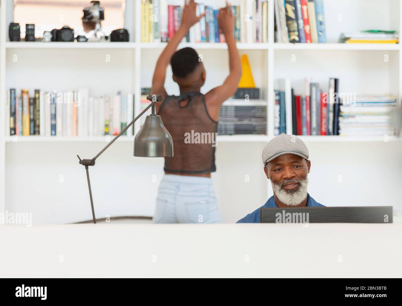 Father using computer and daughter at bookcase in home office Stock Photo