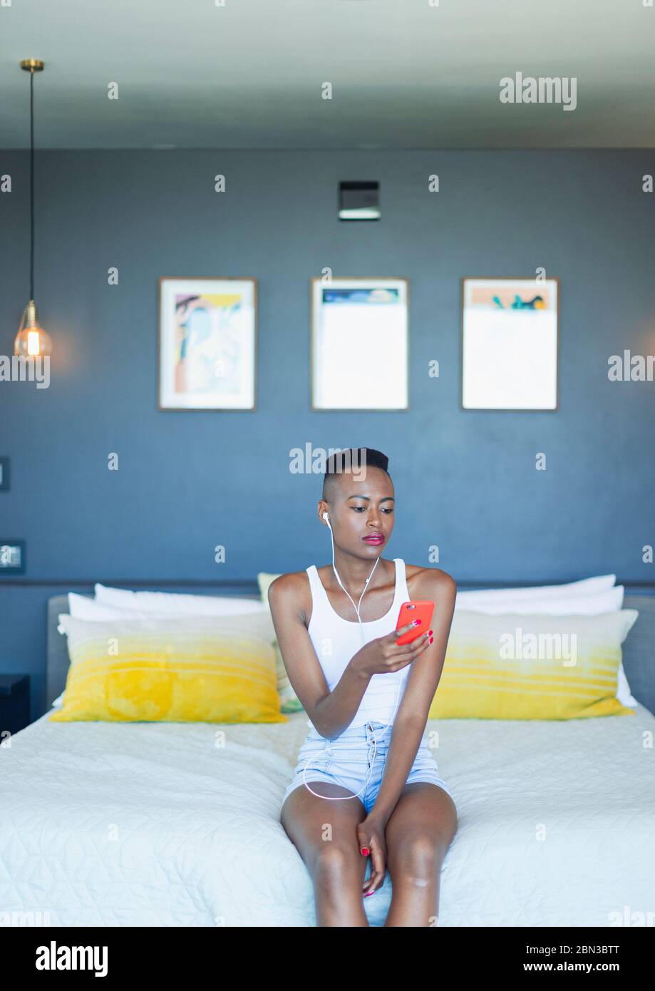 Young woman listening to music with headphones and mp3 player on bed ...