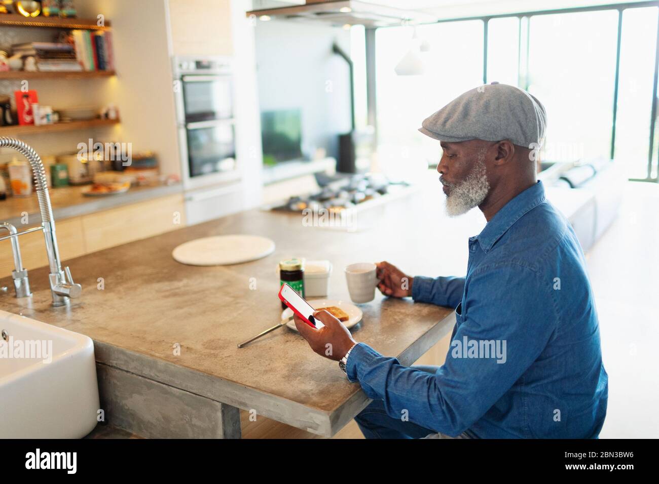 Man enjoying breakfast and using smart phone in morning kitchen Stock Photo