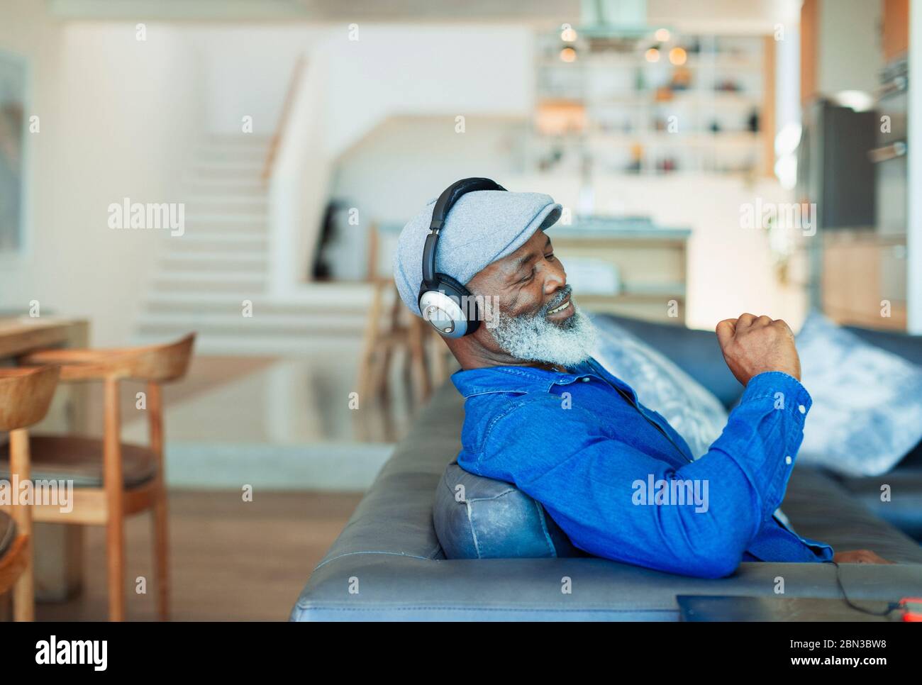 Happy man with headphones listening to music on living room sofa Stock Photo