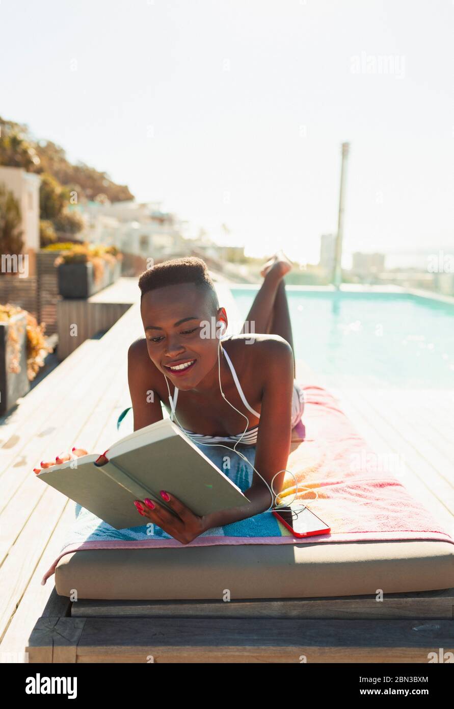 Woman sunbathing, reading book on sunny lounge chair at poolside Stock Photo