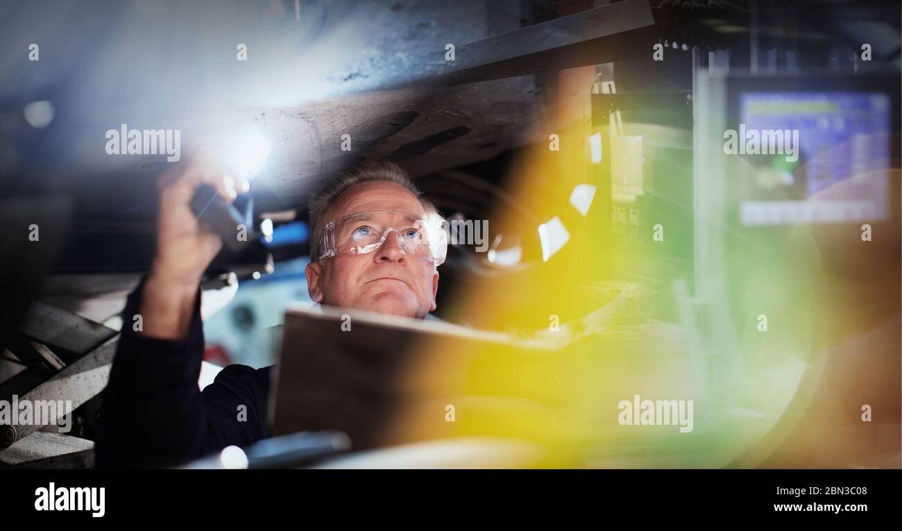 Focused male mechanic with flashlight under car in auto repair shop Stock Photo