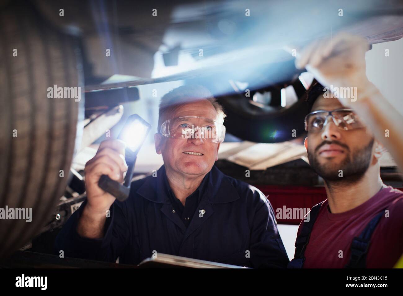 Male mechanics with flashlight working under car in auto repair shop Stock Photo