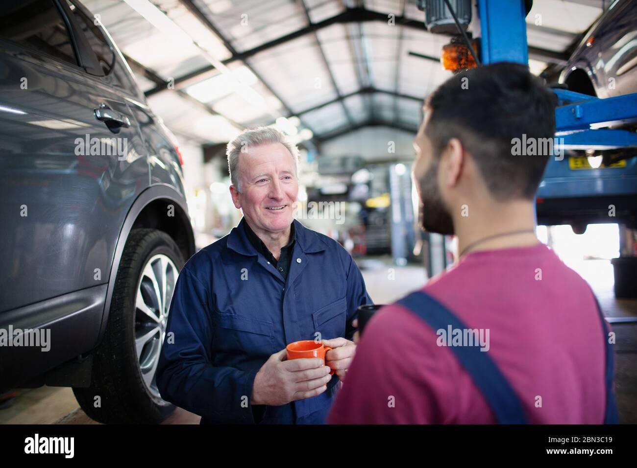 Male mechanics talking and drinking coffee in auto repair shop Stock Photo