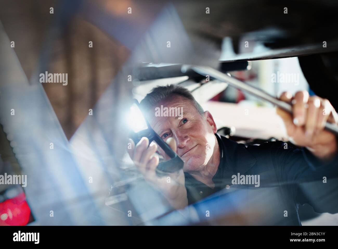 Male mechanic with flashlight working under car in auto repair shop Stock Photo
