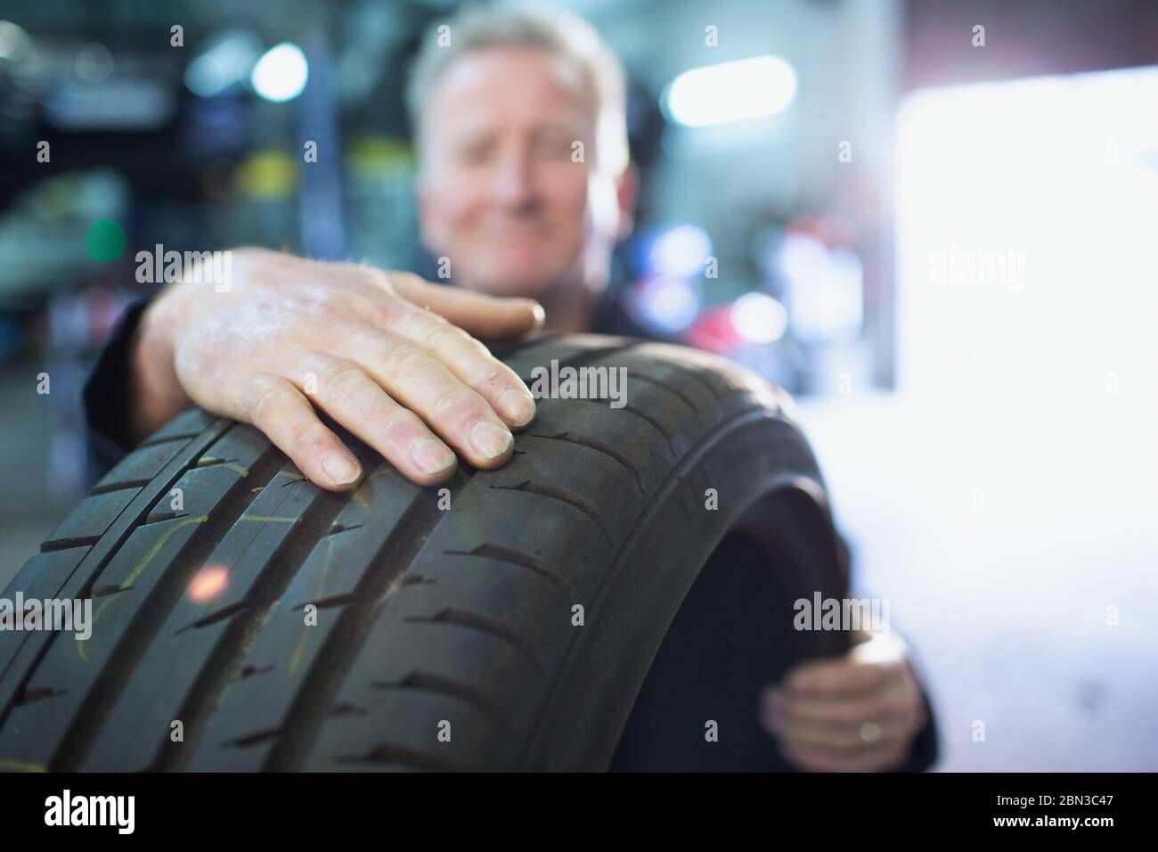 Male mechanic holding tire in auto repair shop Stock Photo
