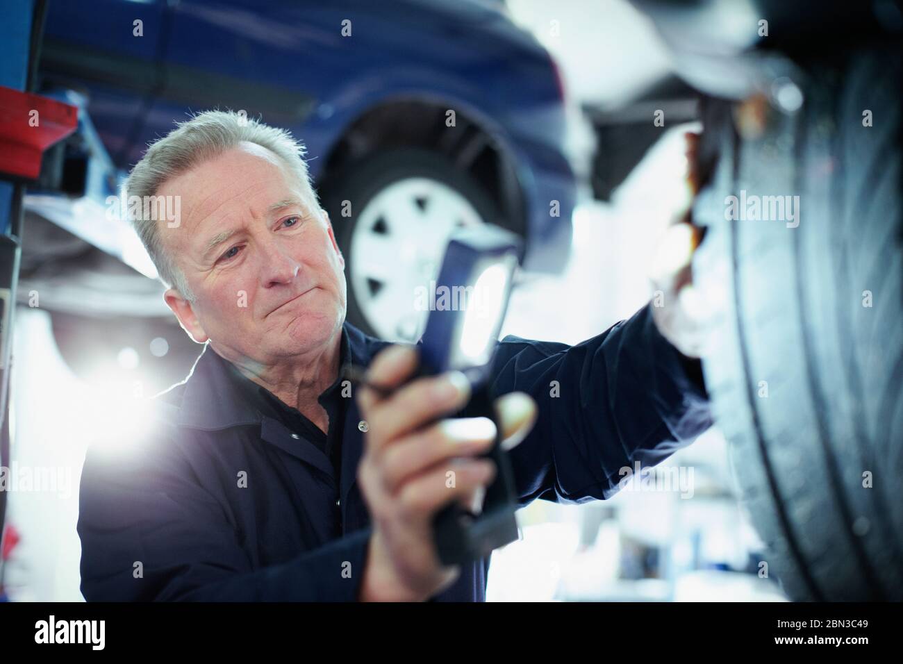 Male mechanic with flashlight examining tire in auto repair shop Stock Photo