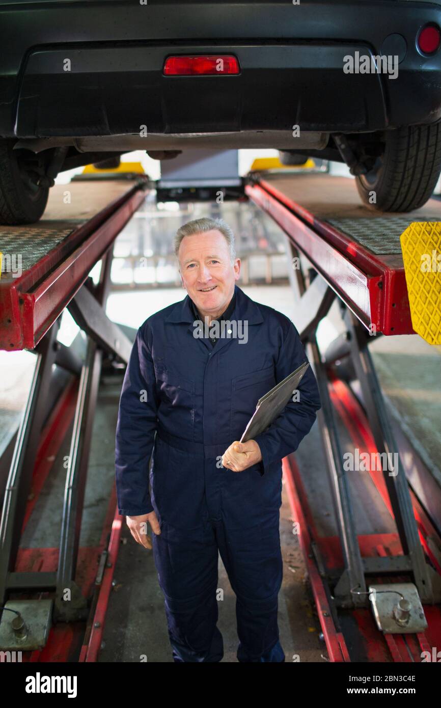 Portrait confident male mechanic under car in auto repair shop Stock Photo