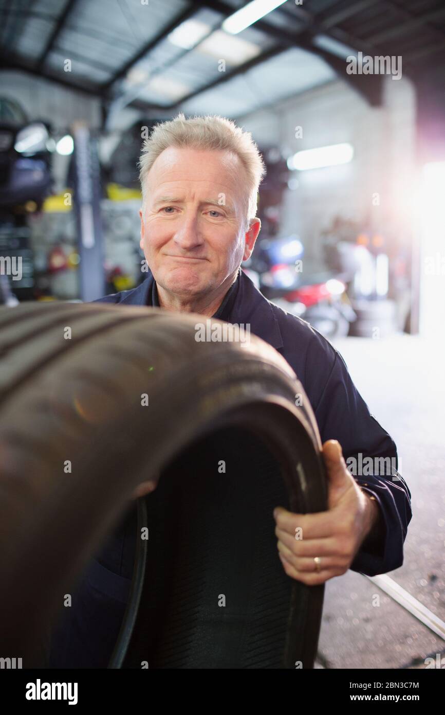 Male mechanic holding tire in auto repair shop Stock Photo