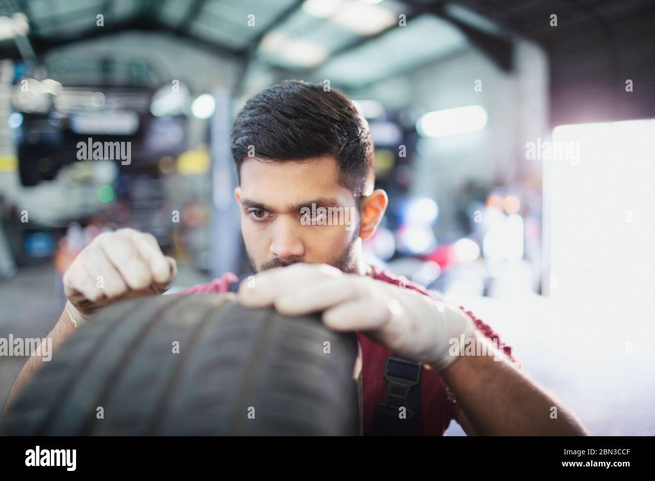 Focused male mechanic examining tire in auto repair shop Stock Photo