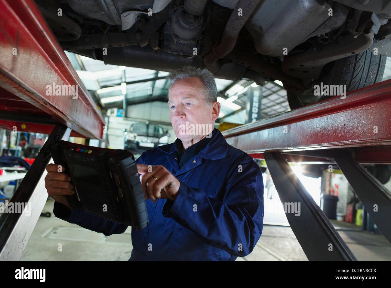 Male mechanic using diagnostic equipment under car in auto repair shop Stock Photo