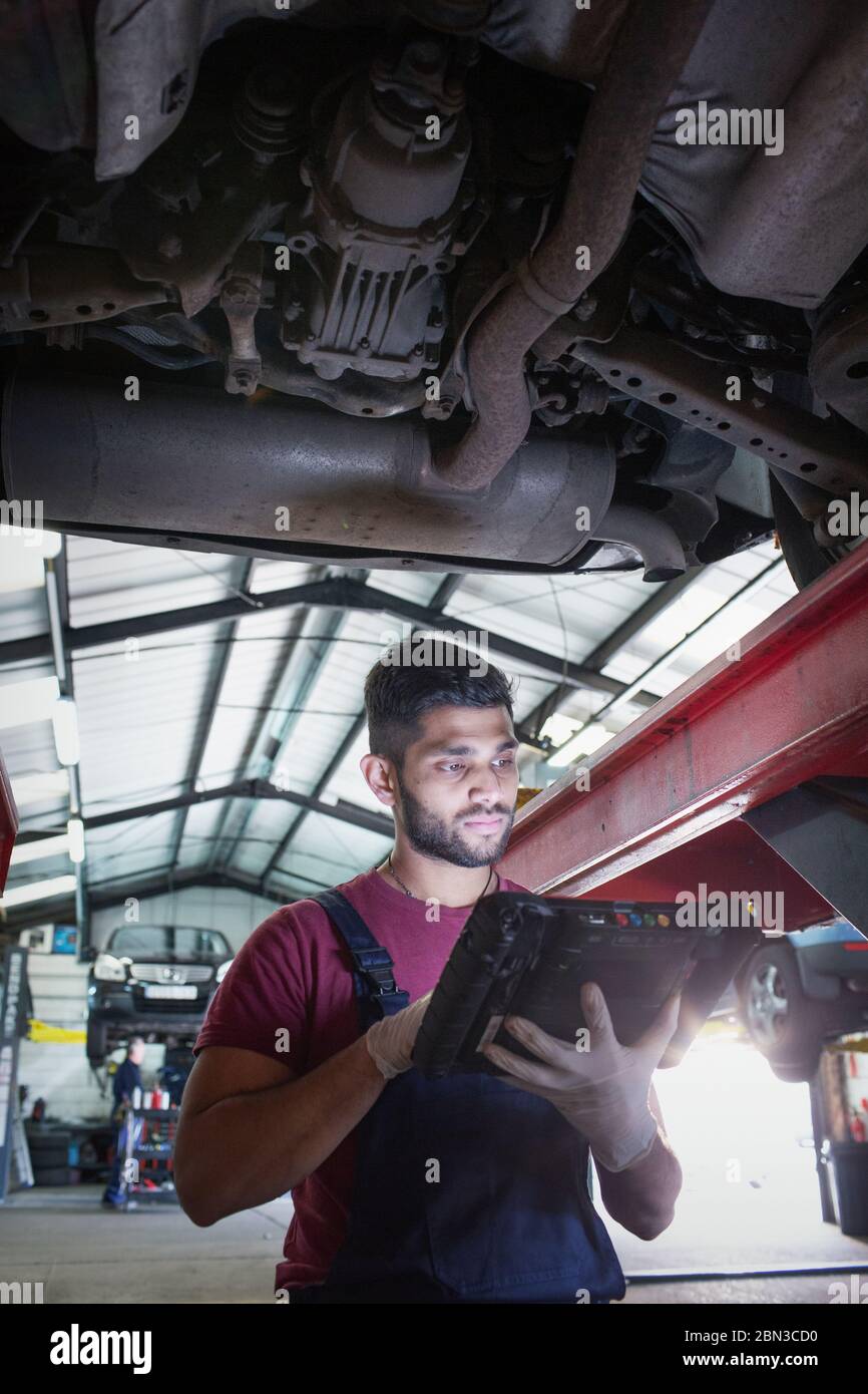 Male mechanic using diagnostic equipment under car in auto repair shop Stock Photo