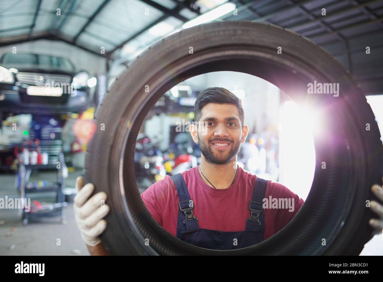 Portrait confident, smiling male mechanic holding tire in auto repair shop Stock Photo