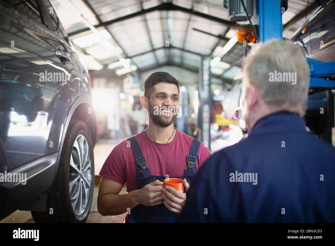 Smiling, happy male mechanics talking and drinking coffee in auto repair shop Stock Photo