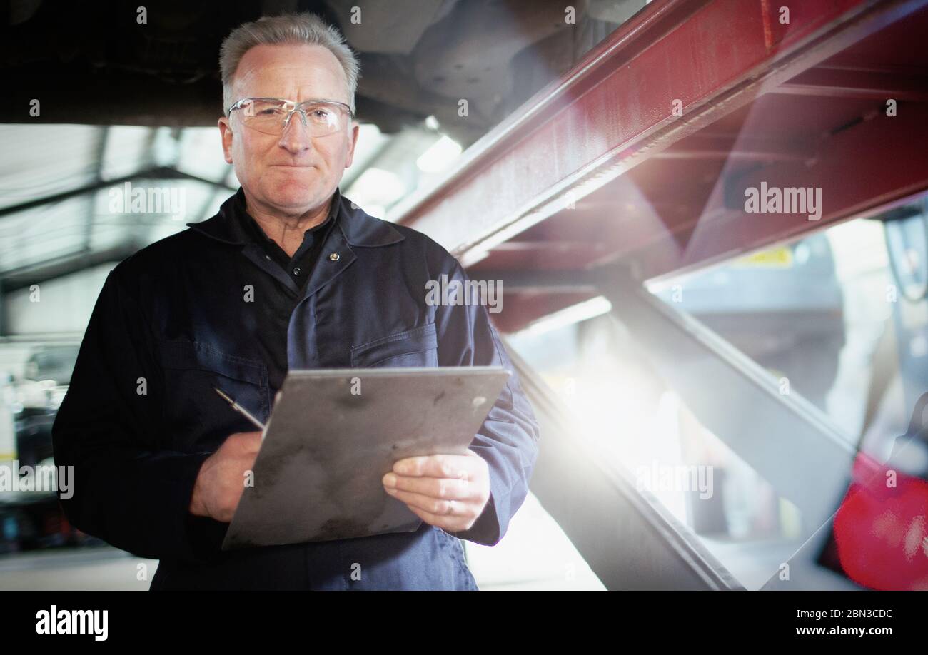 Portrait confident male mechanic with clipboard working under car in auto repair shop Stock Photo