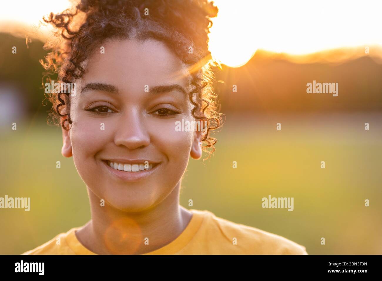 Beautiful biracial mixed race African American teenager teen girl young woman smiling with perfect teeth outside backlit at sunset or sunrise Stock Photo