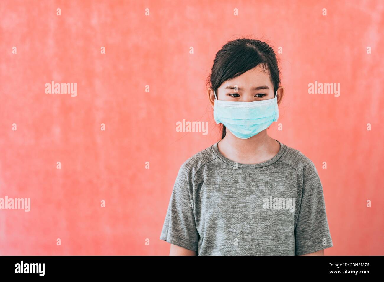 Little asian girl wearing sterile medical mask for protect Covid-19 isolated on red background. Copy space. Stock Photo