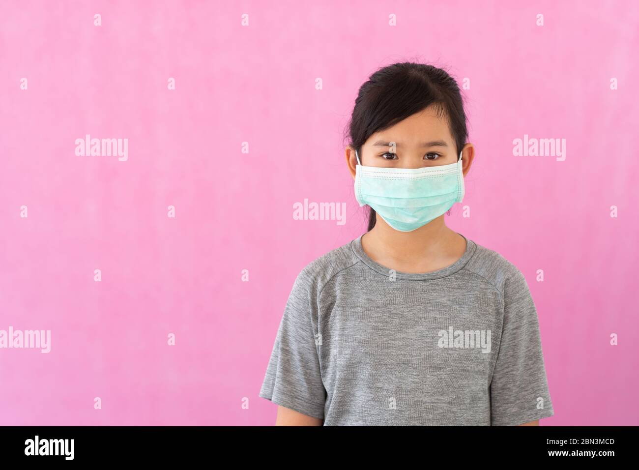 Little asian girl wearing sterile medical mask for protect Covid-19 isolated on pink background. Copy space. Stock Photo