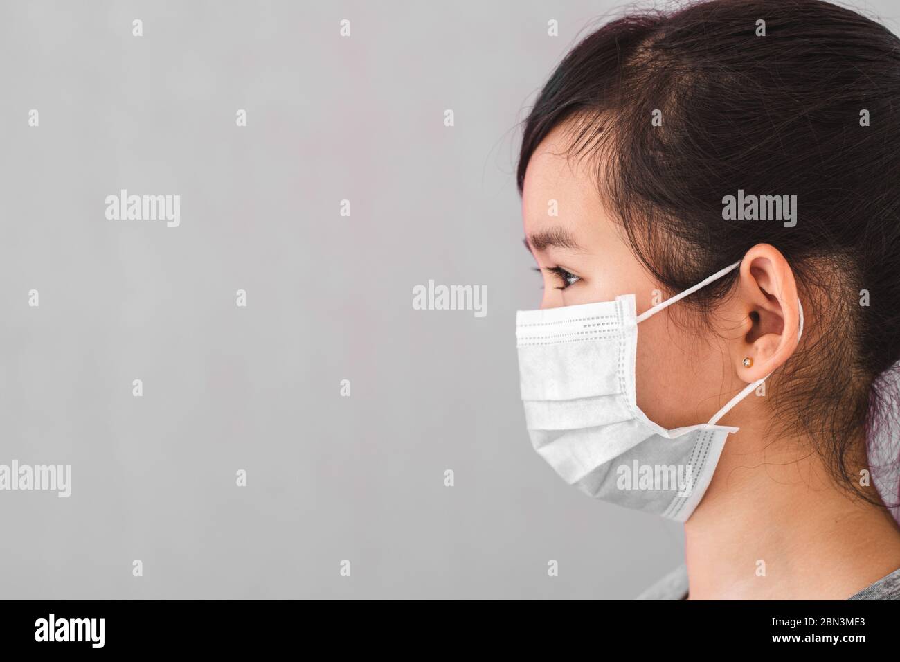 Little asian girl wearing sterile medical mask for protect Covid-19 isolated on gray background. Copy space. Stock Photo