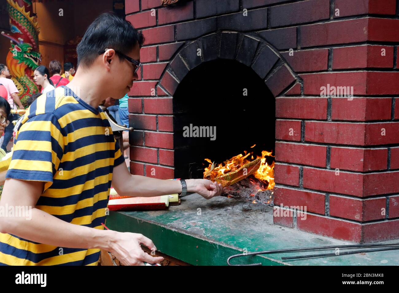 Guan Di chinese taoist temple.  Man burning joss paper offerings in kiln.  Kuala Lumpur. Malaysia. Stock Photo