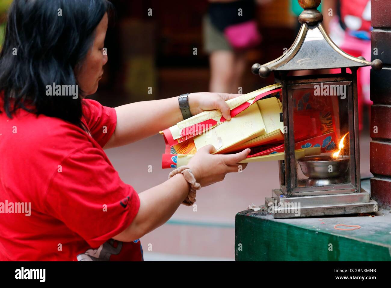 Guan Di chinese taoist temple.  Woman burning joss paper offerings in kiln.  Kuala Lumpur. Malaysia. Stock Photo
