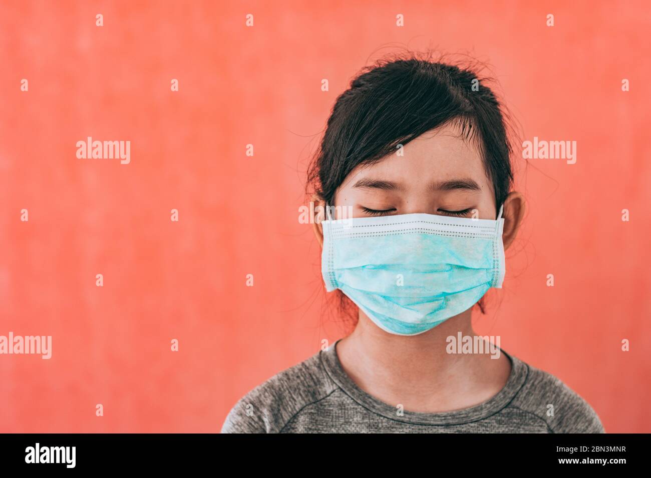 Little asian girl wearing sterile medical mask for protect Covid-19 isolated on red background. Copy space. Stock Photo