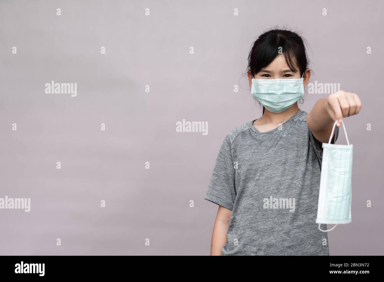 Little girl has sterile medical  mask protect herself from Coronavirus COVID-19 isolated on gray background, child with a mask on her nose for safety Stock Photo