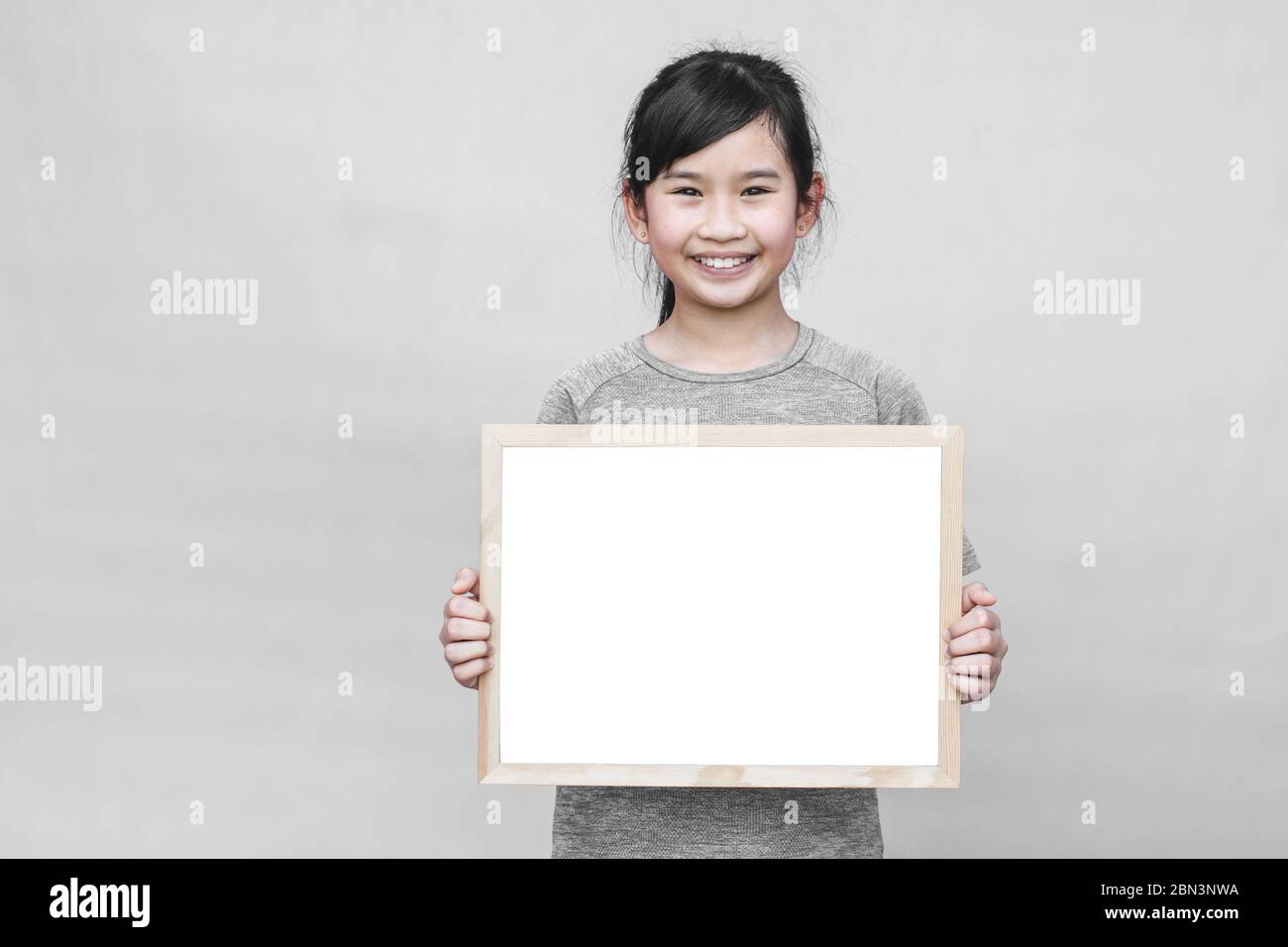 Little asian girl holding whiteboard isolated on gray background. Stock Photo