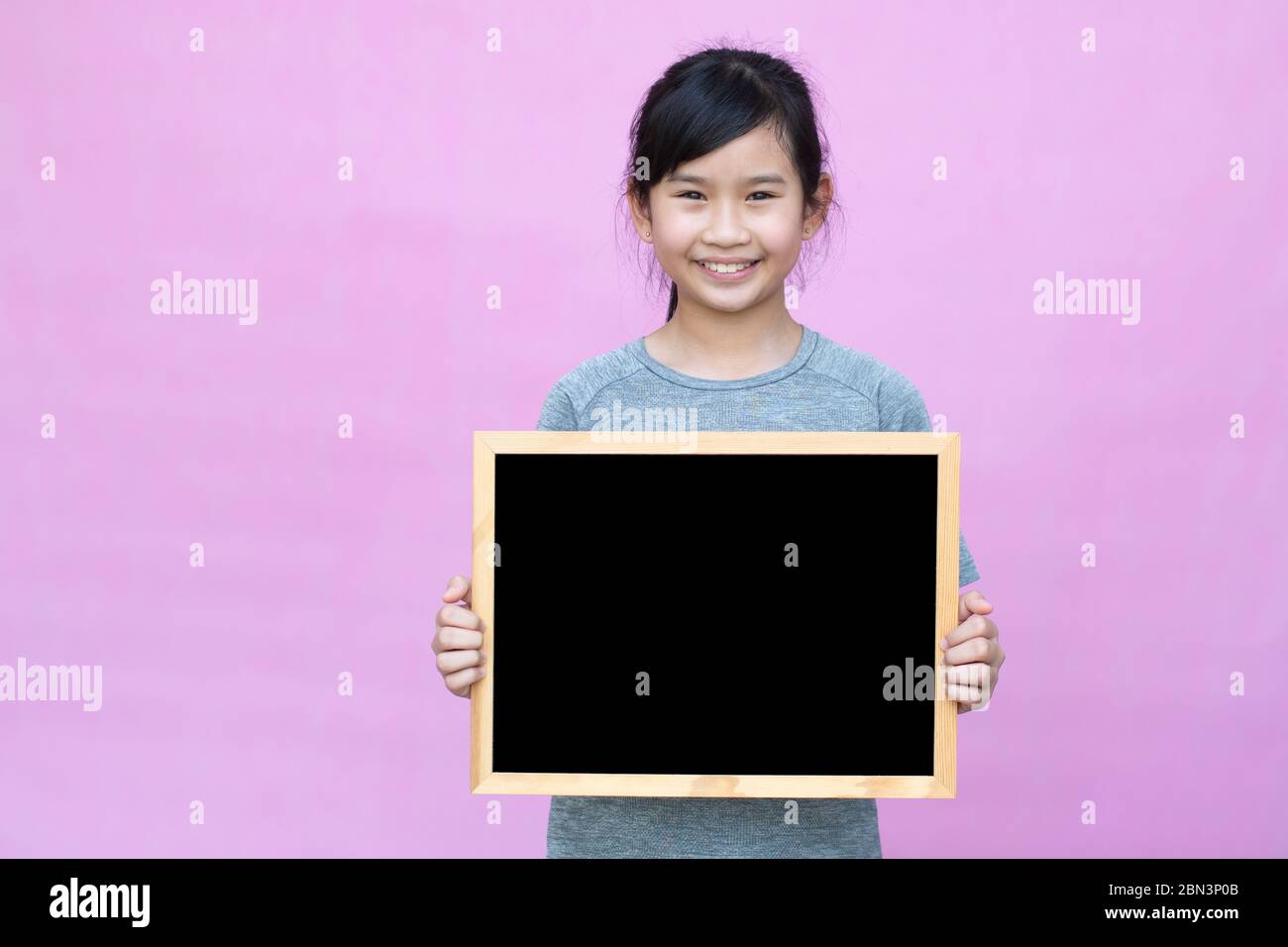 Little asian girl holding blackboard isolated on pink background. Stock Photo