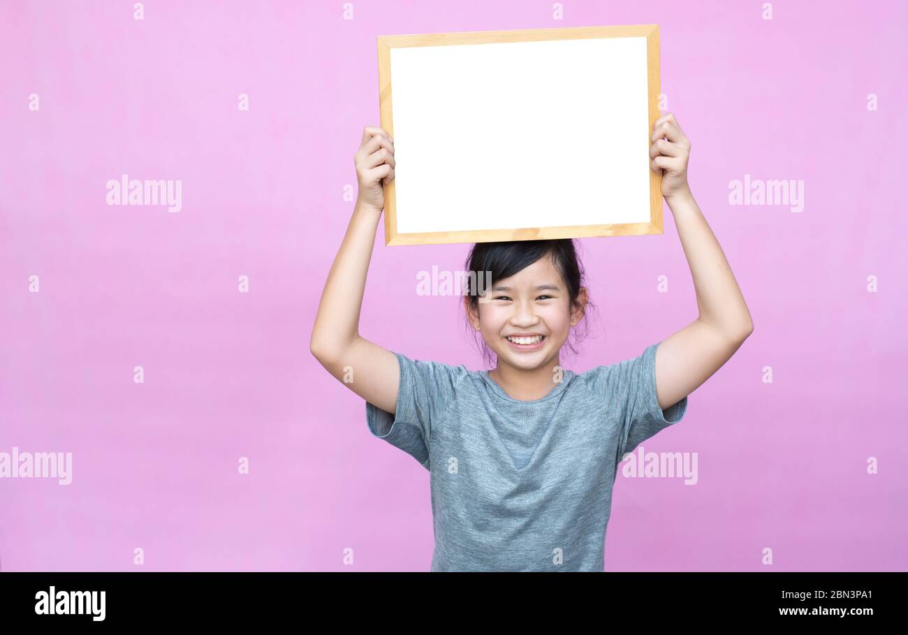 Little asian girl holding whiteboard isolated on pink background. Stock Photo