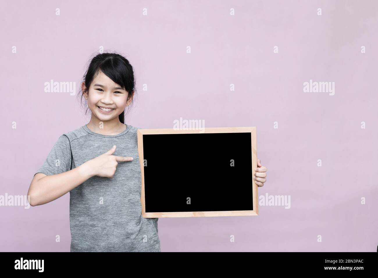 Little asian girl holding blackboard isolated on gray background. Stock Photo