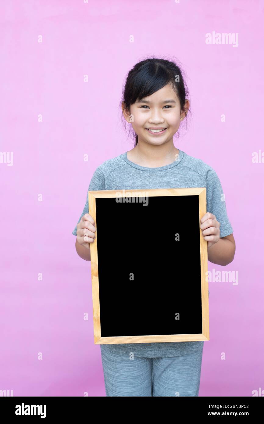 Little asian girl holding blackboard isolated on pink background. Stock Photo