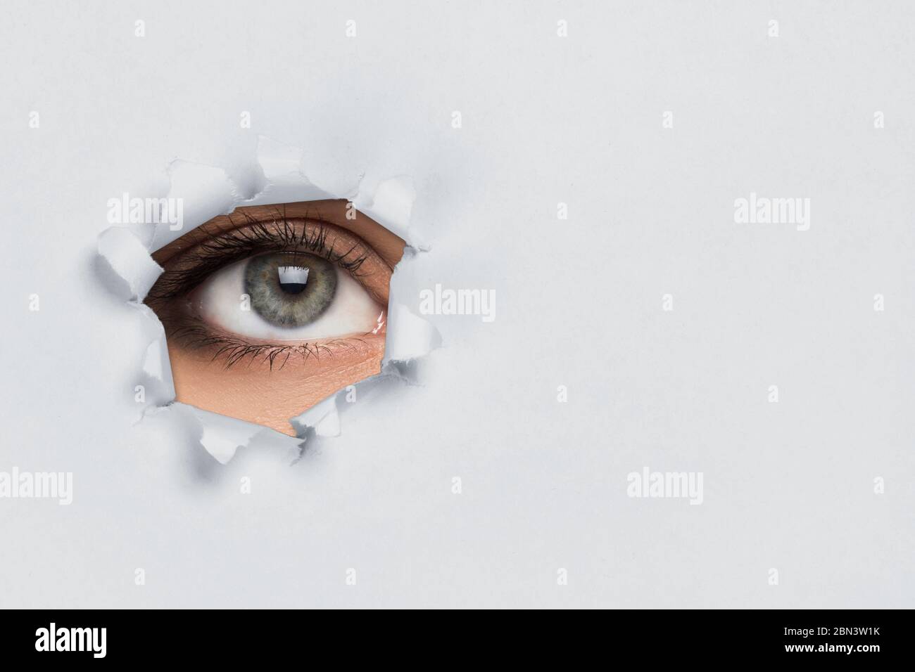 Female eye looking through torn paper Stock Photo