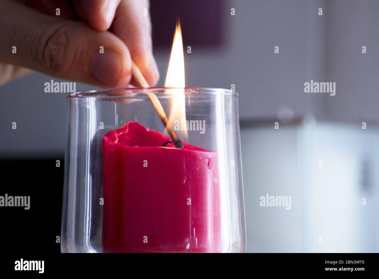 Fingers of man lighting a red candle inside a transparent glass vase