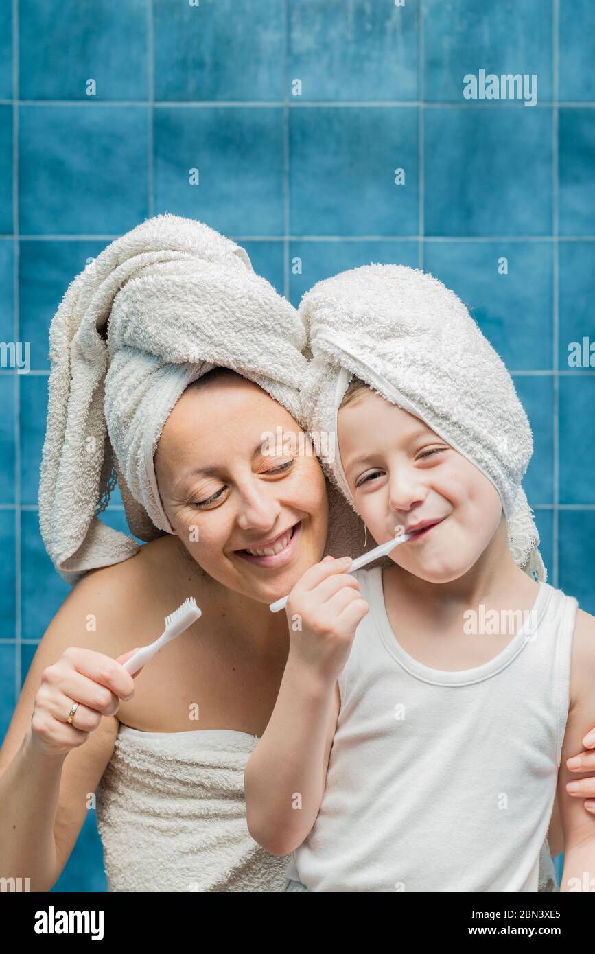 A woman and a boy with towels on their heads brushing their teeth Stock